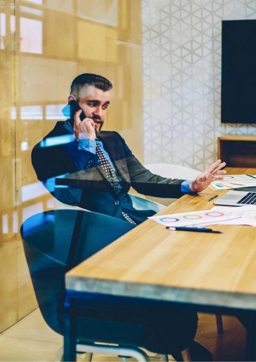 Hiring manager on a phone call at a desk behind a glass wall, representing an employer conducting a backdoor reference check.